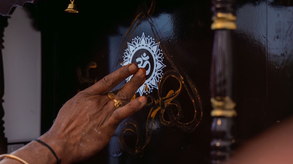 Une main touche un symbole om sur une surface sombre.